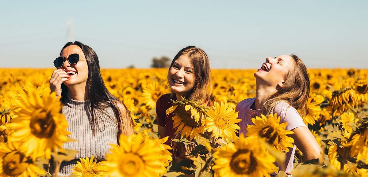 Trzy uśmiechnięte dziewczyny na polu słoneczników.